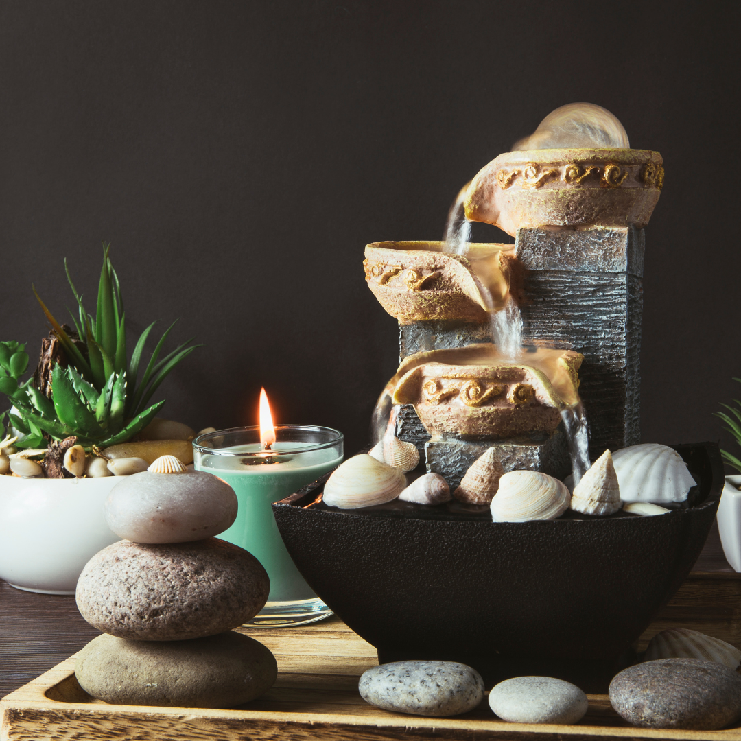 Water feature on a desk with plants and a candle surrounding it